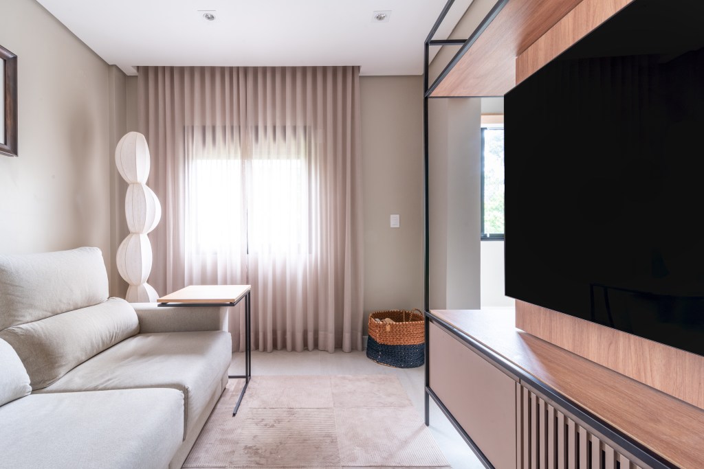 Sala de tv com sofá claro, cortina e luminária