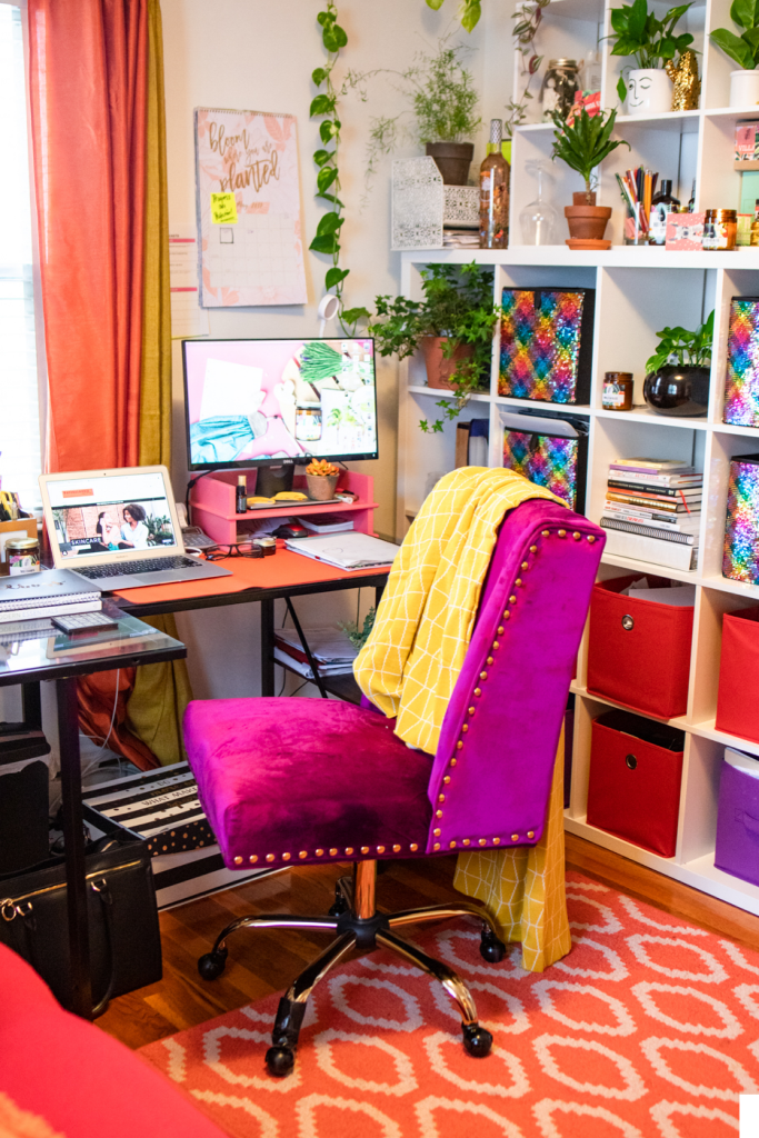 Home office com cadeira pink; tapete estampado; estante com nichos e caixas coloridas