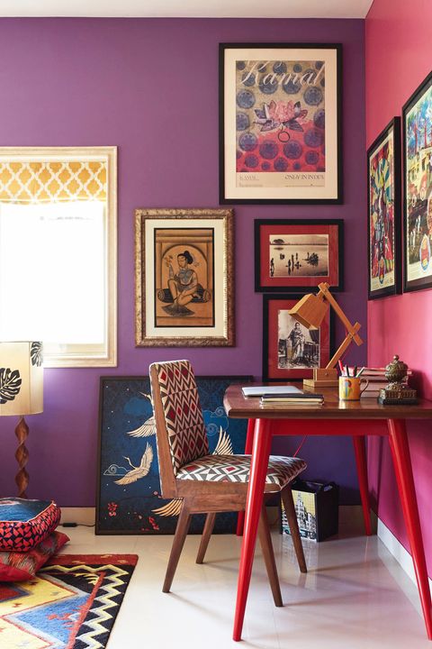 Home office com mesa pequena; uma parede rosa e uma parede roxa com quadros