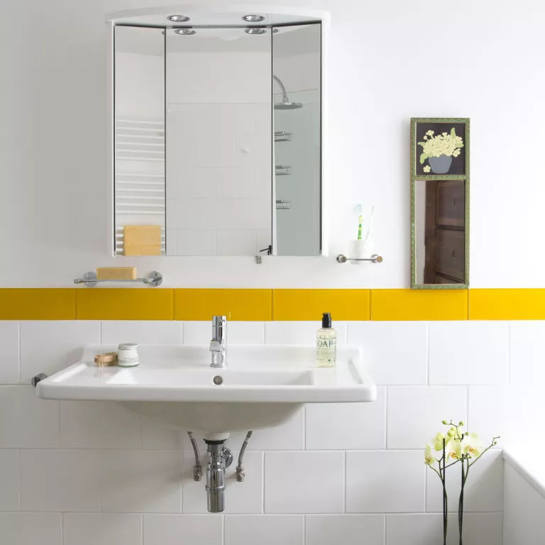 Banheiro com uma faixa de azulejos adesivada de amarelo.