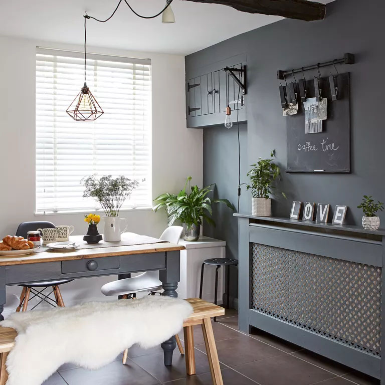 Cozinha com mesa e paredes com decoração em cinza, e um quadro negro acima de um aparador.