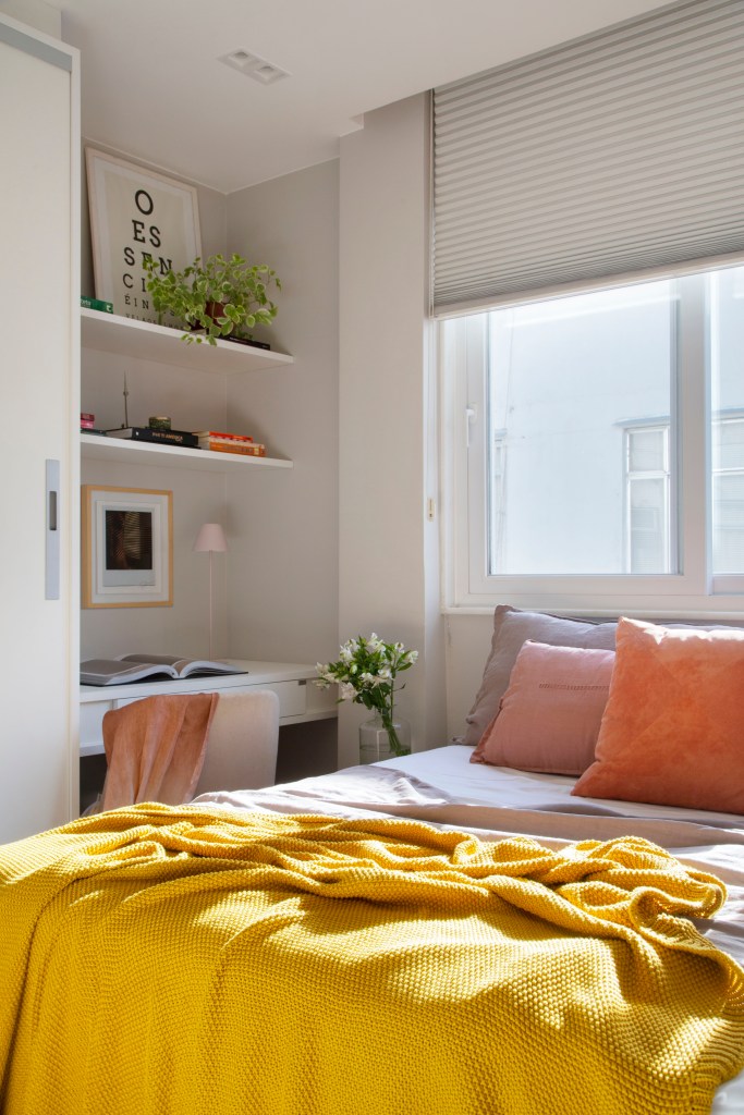 Quarto com cama; manta amarela; pequeno espaço de home office