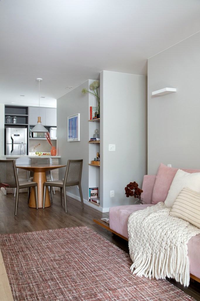 Sala integrada com cozinha; sofá rosa; mesa redonda; cozinha ao fundo