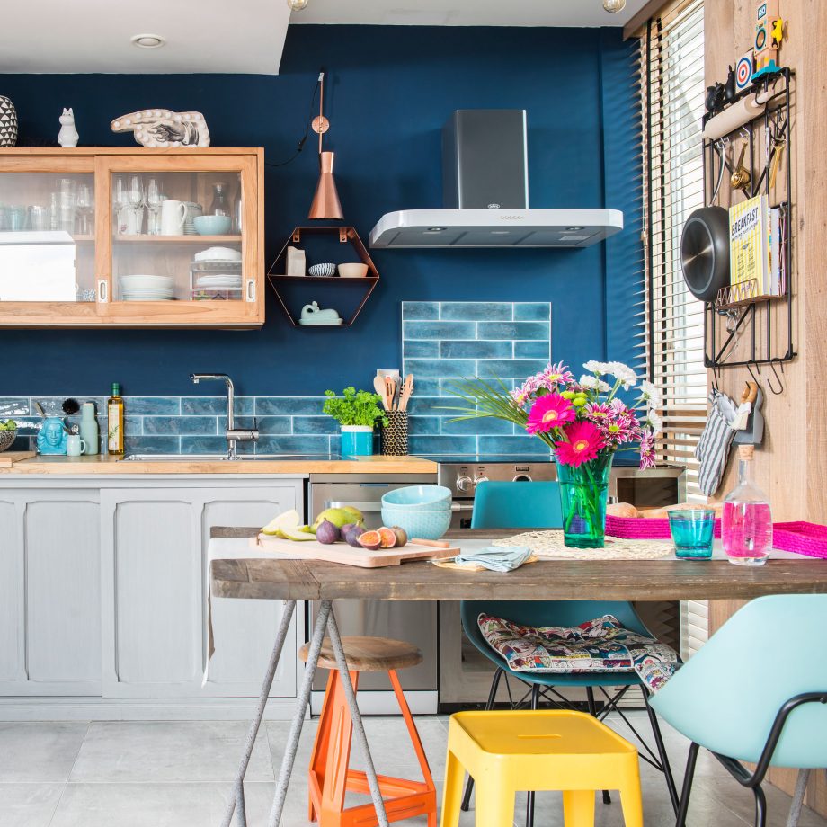 Cozinha contemporânea com parede azul; mesa retangular pequena e cadeiras diferentes