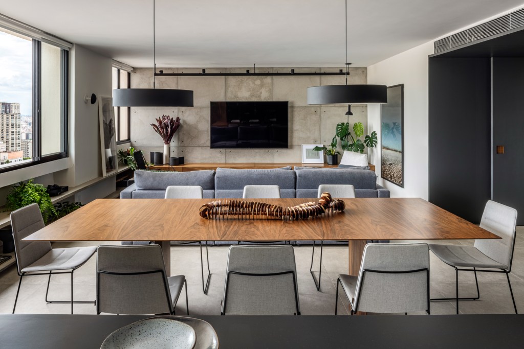 Sala de jantar integrada com estar; mesa em madeira; cadeiras cinzas; sofá azul; tv