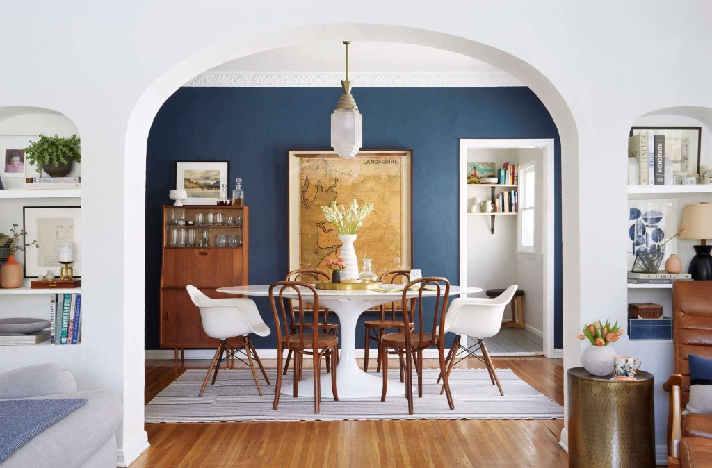 Sala de jantar com parede azul; mesa branca com cadeiras diferentes