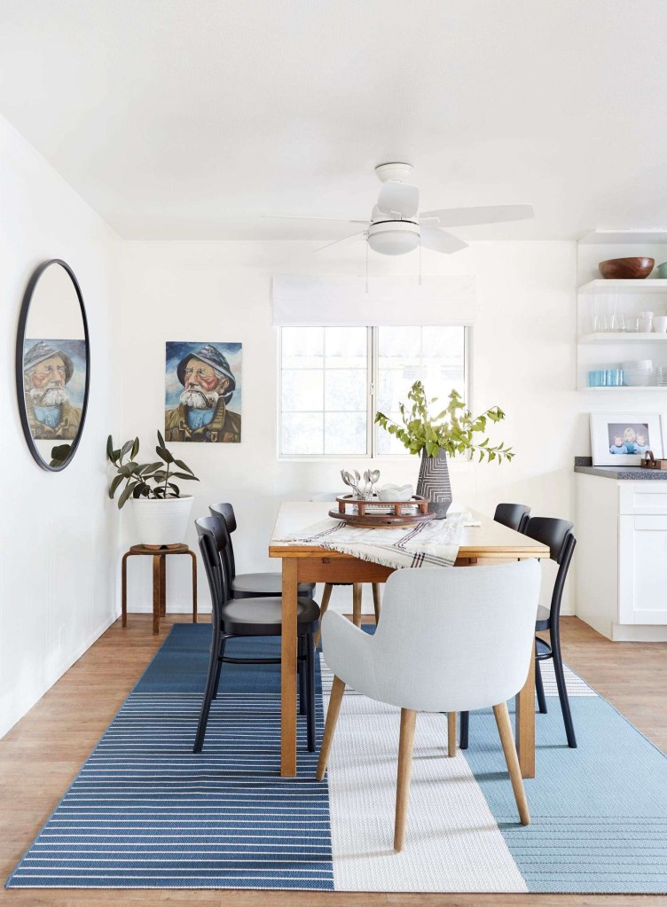 Sala de jantar em tons neutros. tapete azul e espelho circular na parede; mesa em madeira; cadeiras de modelos diferentes