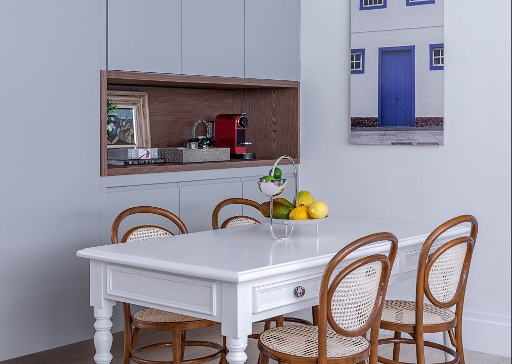 Cozinha com armários azuis, quatro na parede lateral, mesa branca com quatro cadeiras ao seu redor.