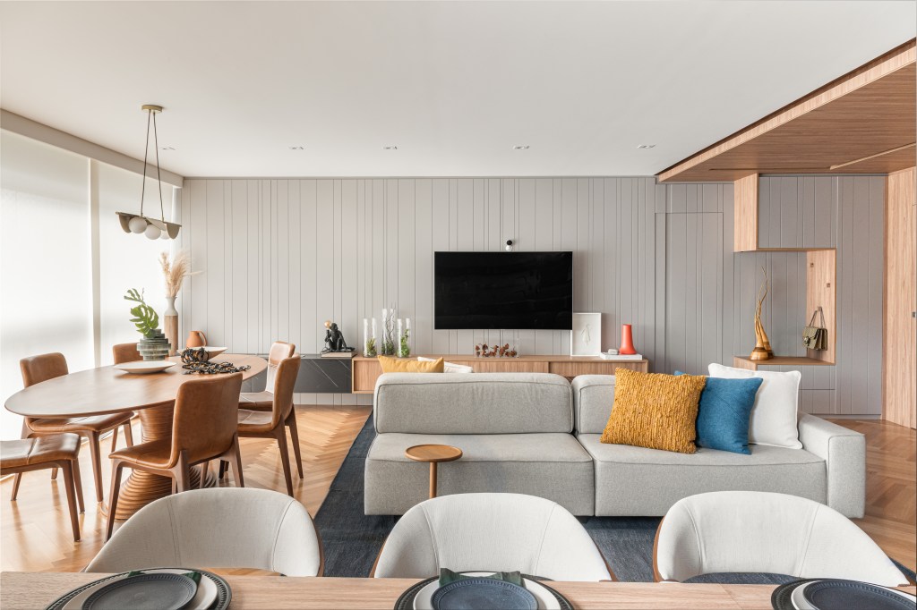 Sala de estar integrada com jantar e tv; mesas em madeira; sofá cinza; tv em painel de marcenaria cinza