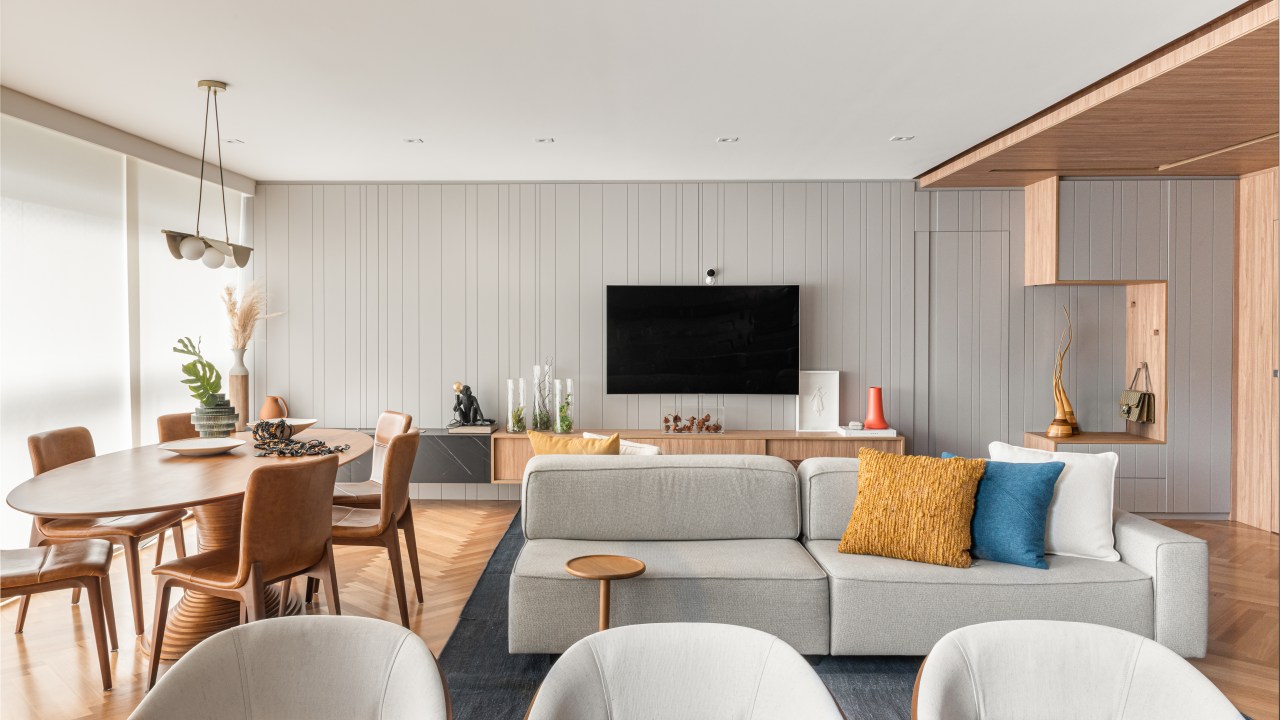 Sala de estar integrada com jantar e tv; mesas em madeira; sofá cinza; tv em painel de marcenaria cinza