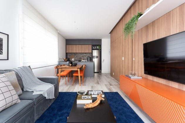 Sala de estar integrada à cozinha, com longa parede revestida de madeira.