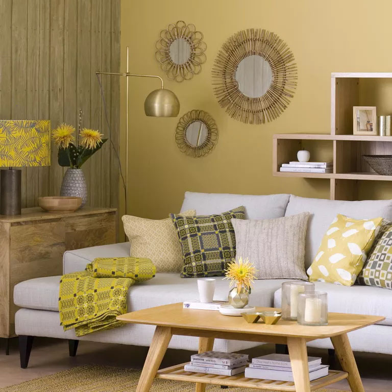 Sofá branco em frente a uma parede amarela, com uma mesa de centro de madeira, prateleiras e espelhos ao fundo.