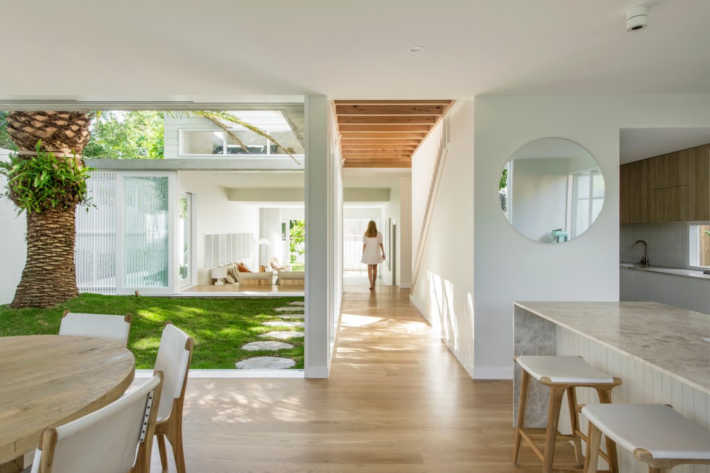 Foto mostra área da sala de jantar e cozinha, com piso de madeira e mobiliário claro, com pátio interno integrado e muita luz natural.