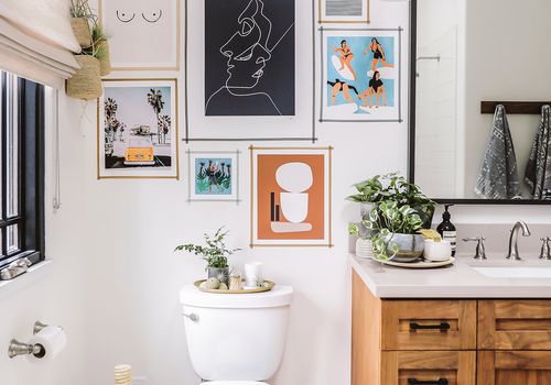 Banheiro com quadros na parede acima do vaso sanitário