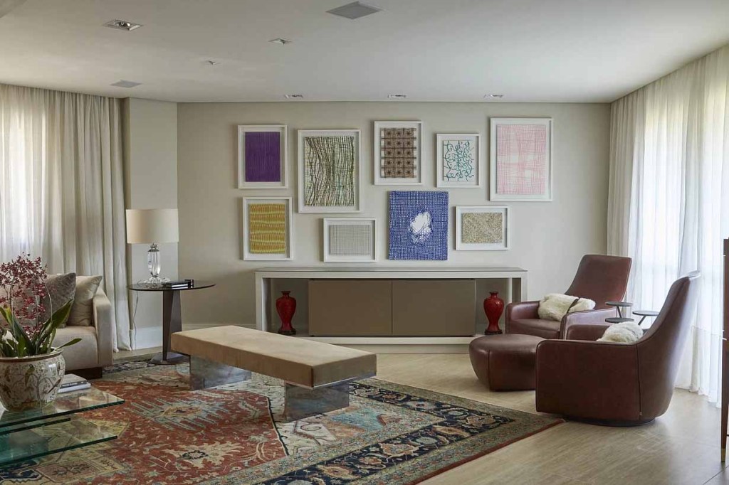 residencia MET- Anna Loyola Sala espaçosa, com poltronas, um grande aparador, quadros pendurados em uma parede em leve tom de cinza.