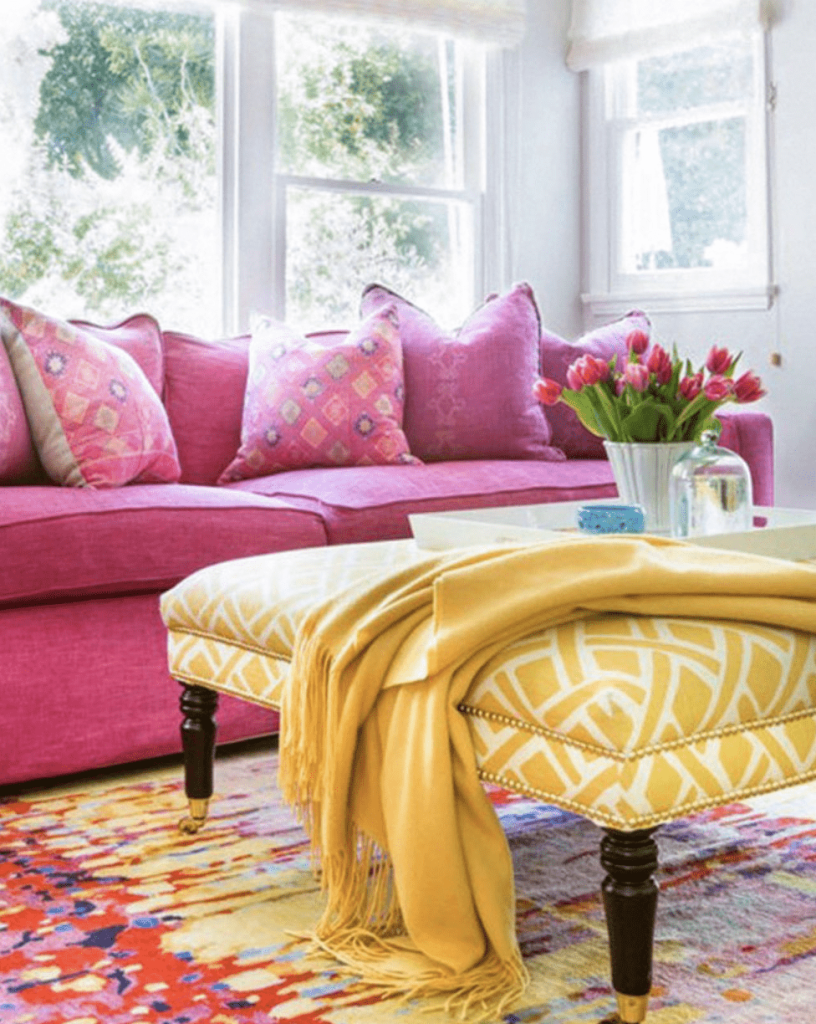Sala de estar com sofá rosa, tapete colorido, com mesa de centro com tecido amarelo.