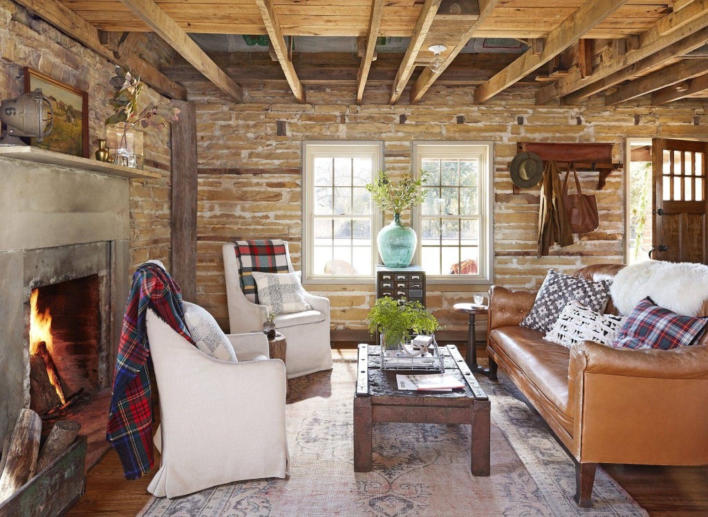 Sala de estar em estilo country chic com paredes de tijolos, sofá marrom de couro, vigas aparentes no teto.