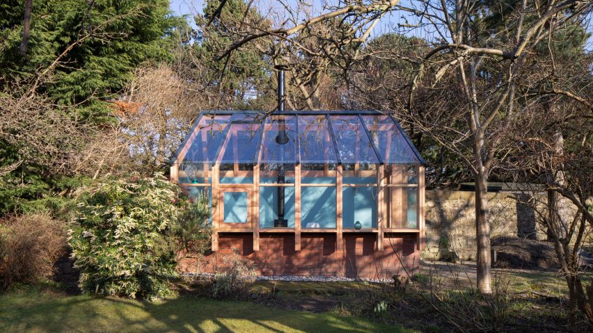 Fachada de construção com base de tijolos e estrutura de madeira em cima, com telhas translúcidas em um jardim