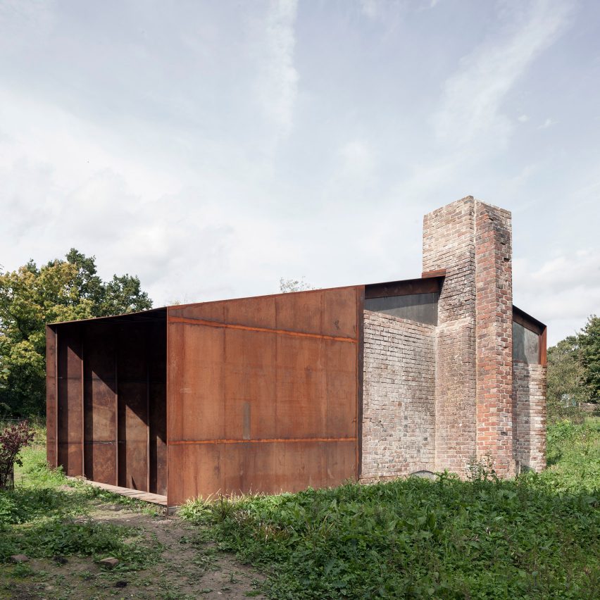 Fachada de construção com parte em tijolos e parte em aço corten, em uma área verde.