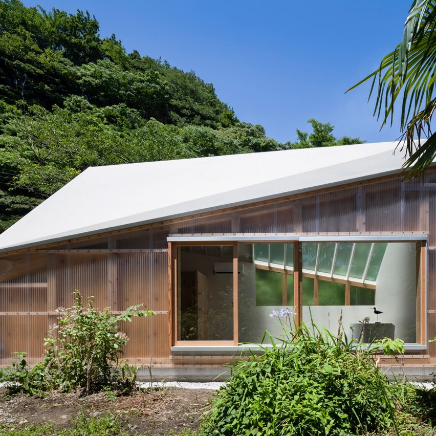 Fachada de estúdio em madeira com abertura frontal em vidro e recortes geométricos na cobertura de cor bem clara, com jardim na frente.