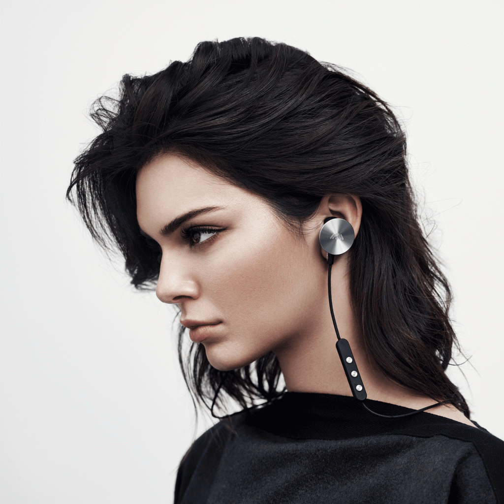 Mulher jovem usa fones de ouvido intra-auriculares com parte externa acabadas em metal escovado.