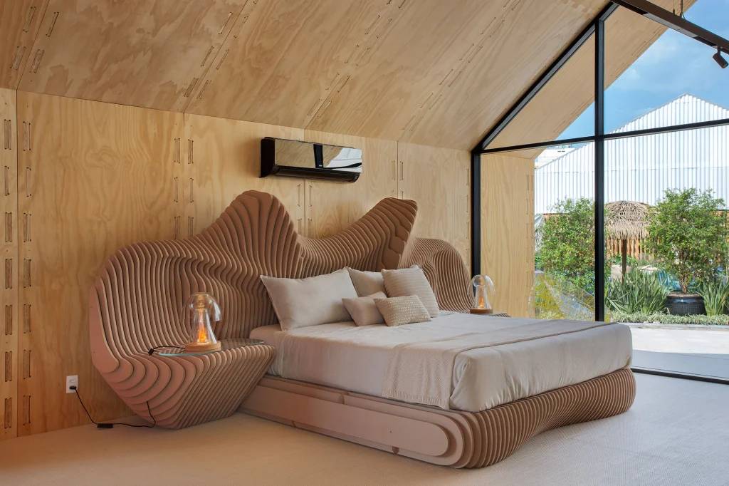 Quarto com cama de casal desenhada em madeira engenheirada em formato orgânico, com paredes de madeira e abertura de vidro.