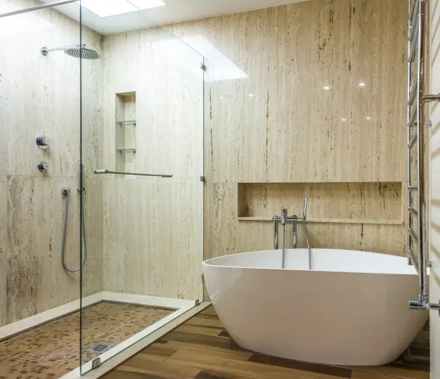 Banheiro com banheira de imersão branca e, na lateral, um box de vidro na área do chuveiro.