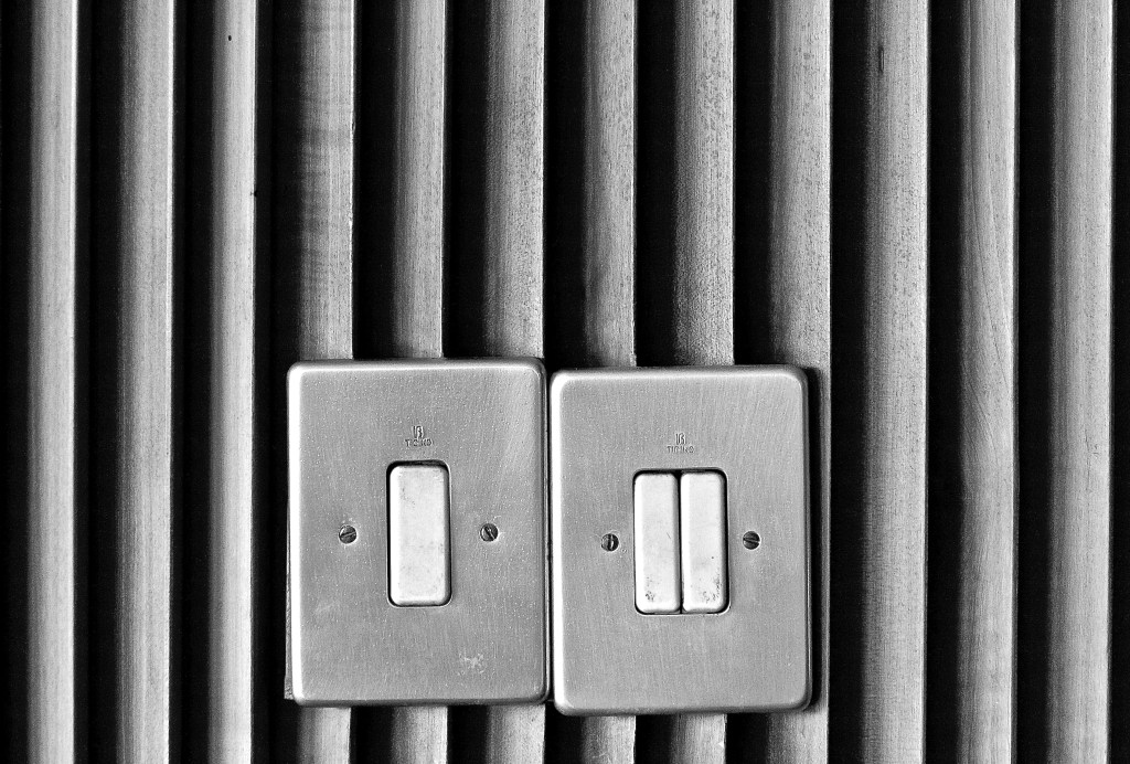 Imagem mostra dois interruptores em parede com persiana, sendo um com um botão e o outro com dois botões de liga e desliga.