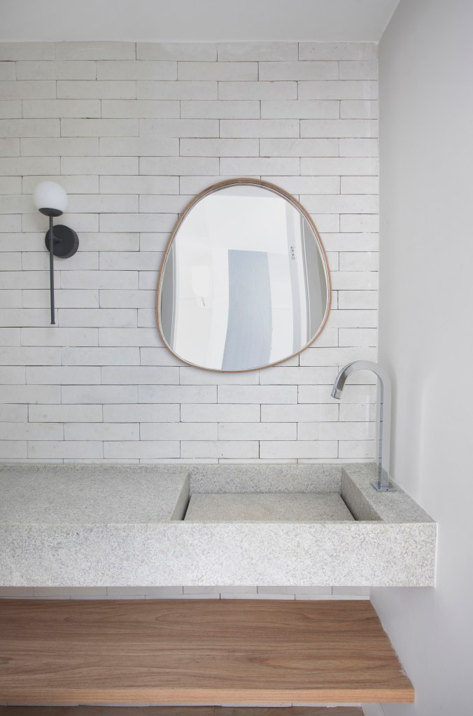 Banheiro com azulejos brancos e espelho com forma orgânica