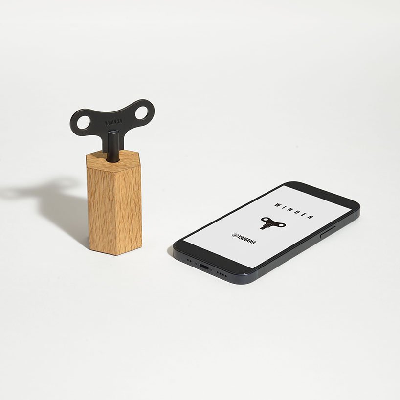 Pequeno objeto que consiste em uma chave preta encaixada em um bloco de madeira. Ao lado, um smartphone.