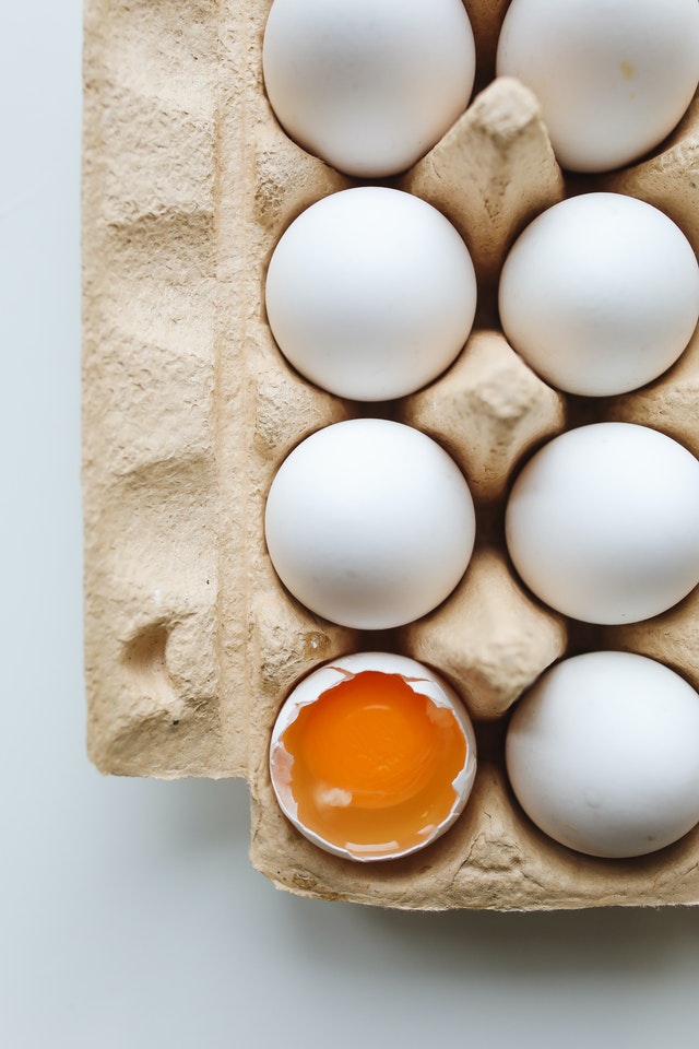 Caixa de ovos cheia com um ovo sem metade da casa, deixando à mostra a gema e a clara.