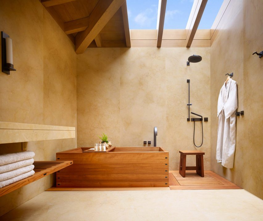 Banheiro em tons terrosos com grande claraboia e banheira de madeira em estilo japonês.