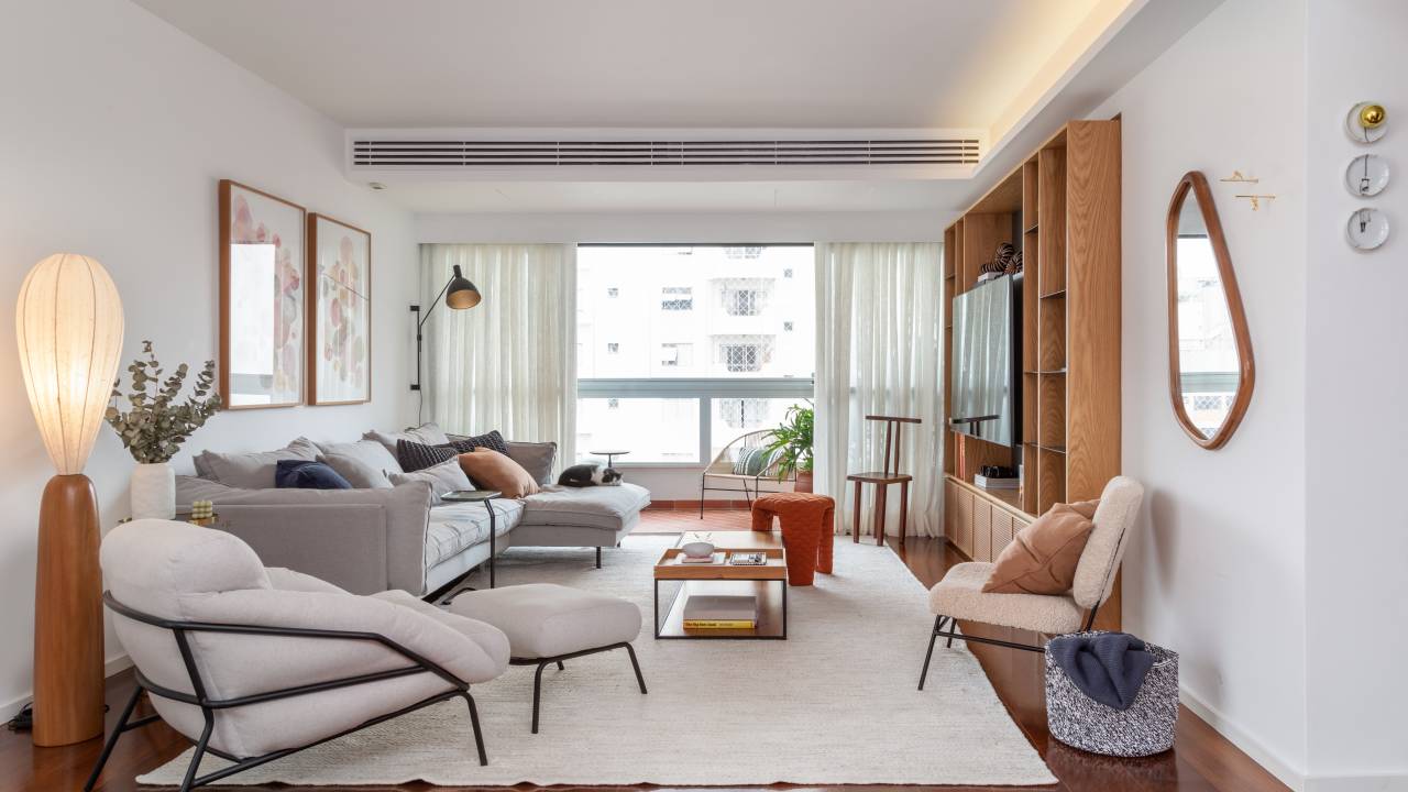 Sala de estar com sofás e poltronas; móvel em madeira com tv; tapete branco