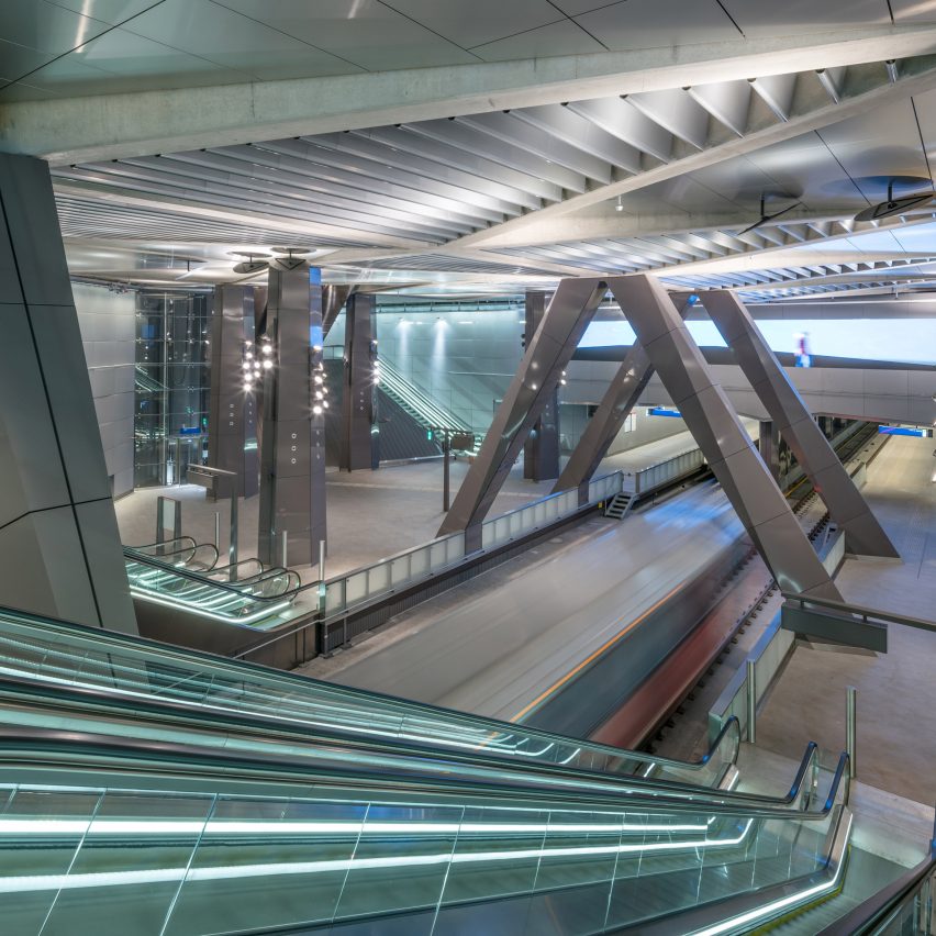 Estação de metrô com escadas rolantes e iluminação linear, grandes colunas em 