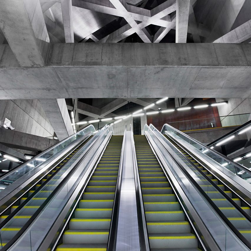 Escadas rolantes vistas de baixo para cima, com teto em vigas de concreto formando uma espécie de trama.