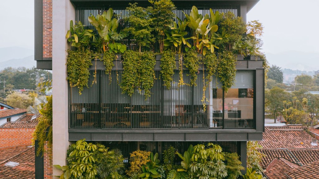 Detalhe da fachada mostra floreiras com plantas tropicais nas varandas.
