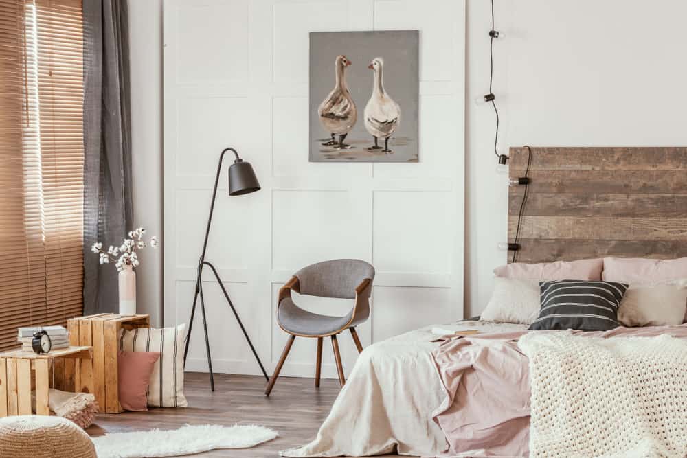 Quarto rústico com pintura de aves na parede; cama com cabeceira de madeira; cadeira e luminária de piso