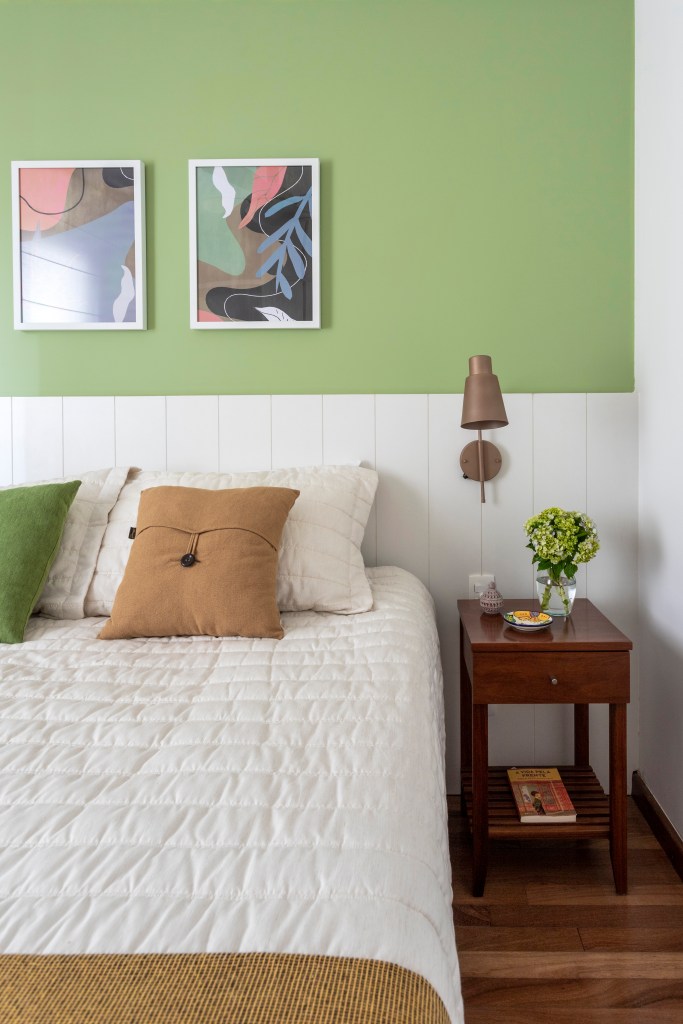 Quarto com cama; cabeceira em madeira branca; mesinha lateral; parede verde