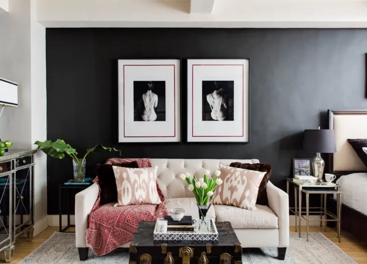 Sala de estar com sofá branco e parede preta, quadros pendurados
