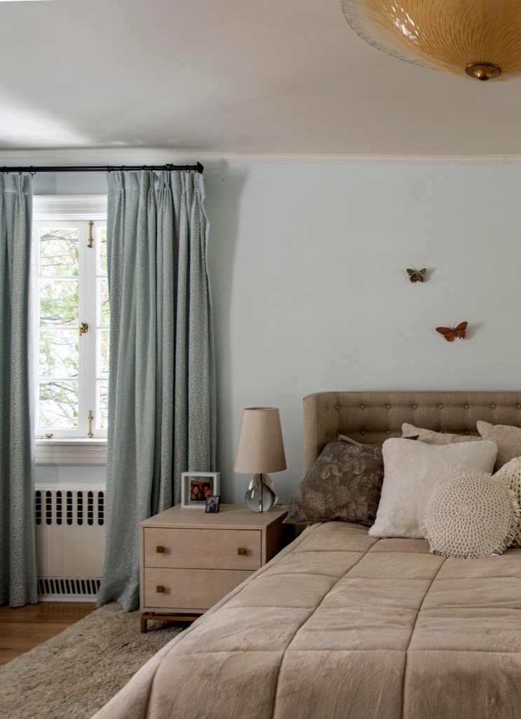 Quarto de casal com cortinas azuis, mesa de cabeceira de madeira e cama com cabeceira. Borboletas na parede