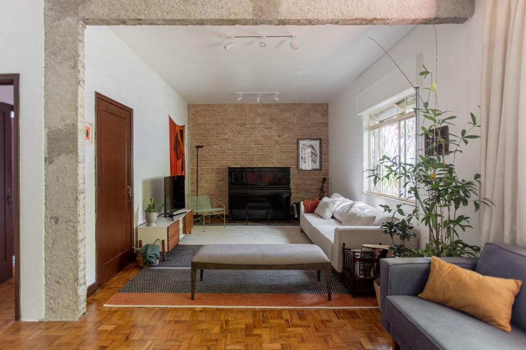 Sala de estar integrada com parede de tijolos ao fundo, banco e sofá brancos