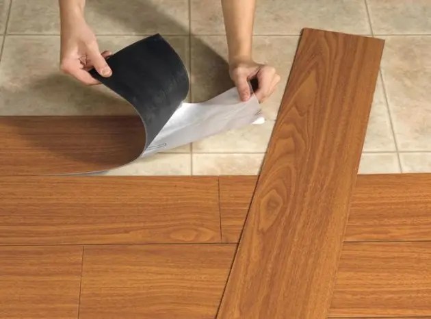 Detalhe de mãos aplicando laminado adesivo sobre piso existente.