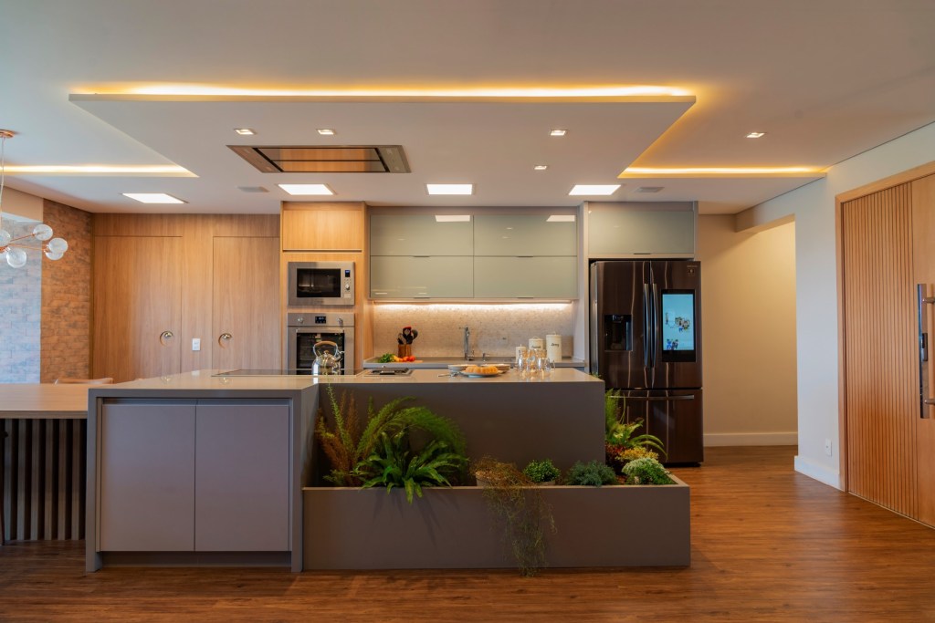 Cozinha integrada com iluminação em spots no teto e fitas de led nos móveis.
