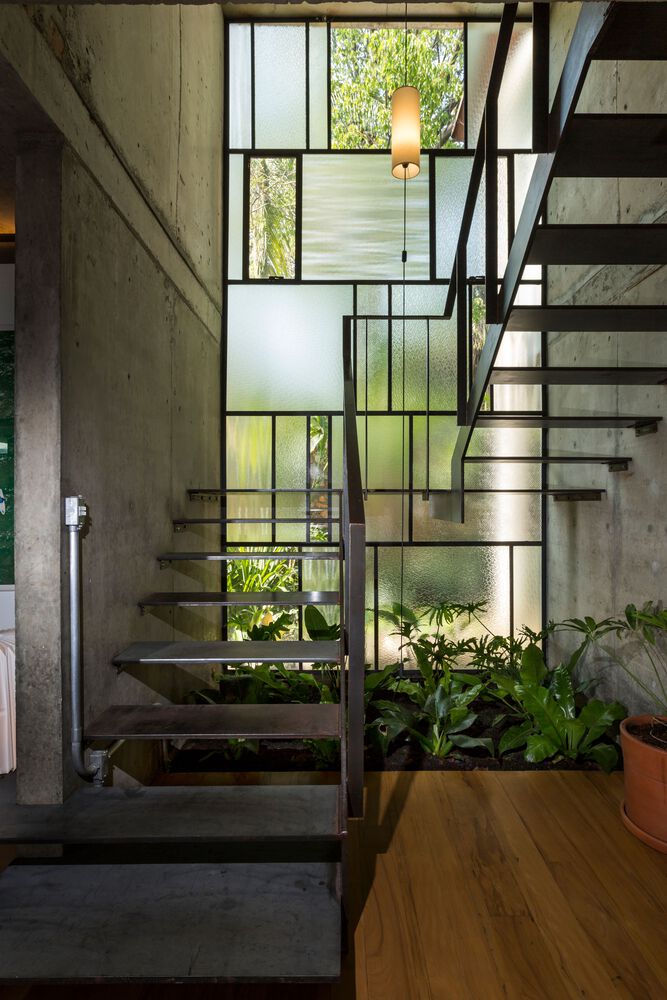 Escada metálica interna tem parede de vitral que amplia a luz natural e permite manter um jardim de inverno.