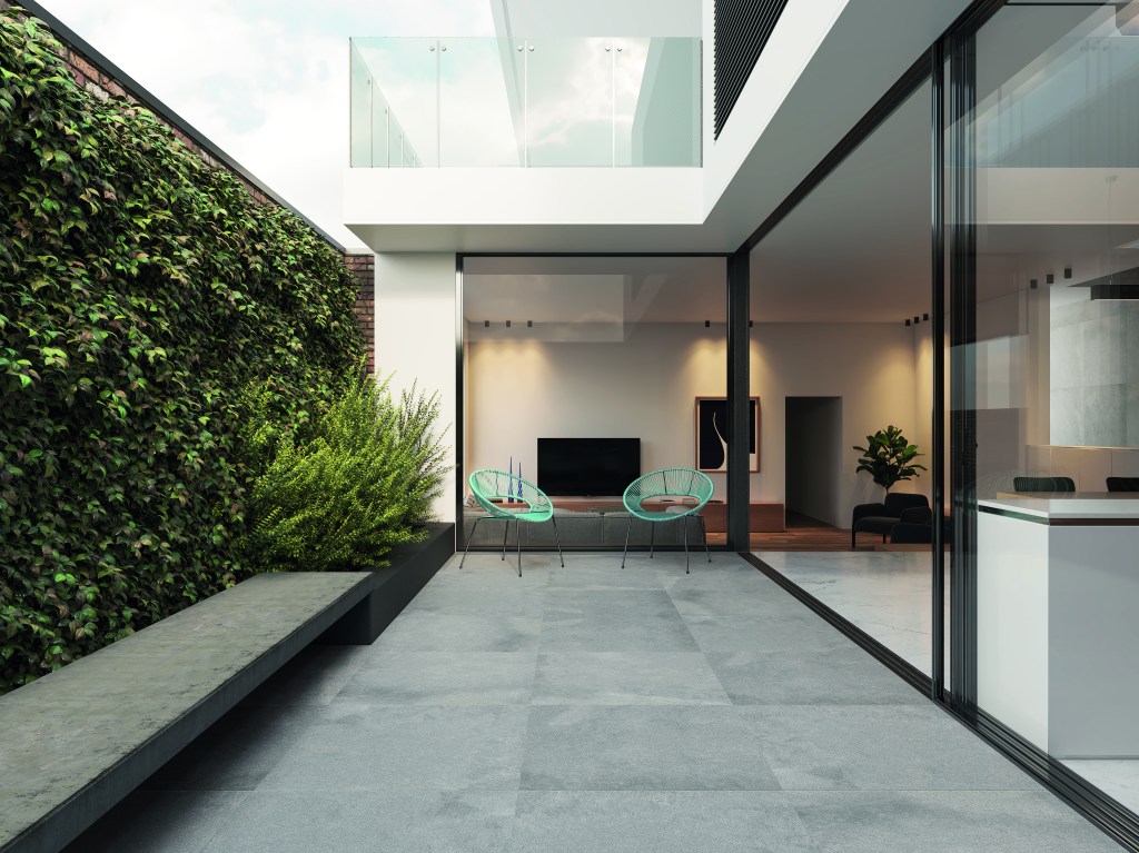 Varanda de casa tem piso de porcelanato fosco antideslizante, parede coberta por vegetação e integração com área de estar.