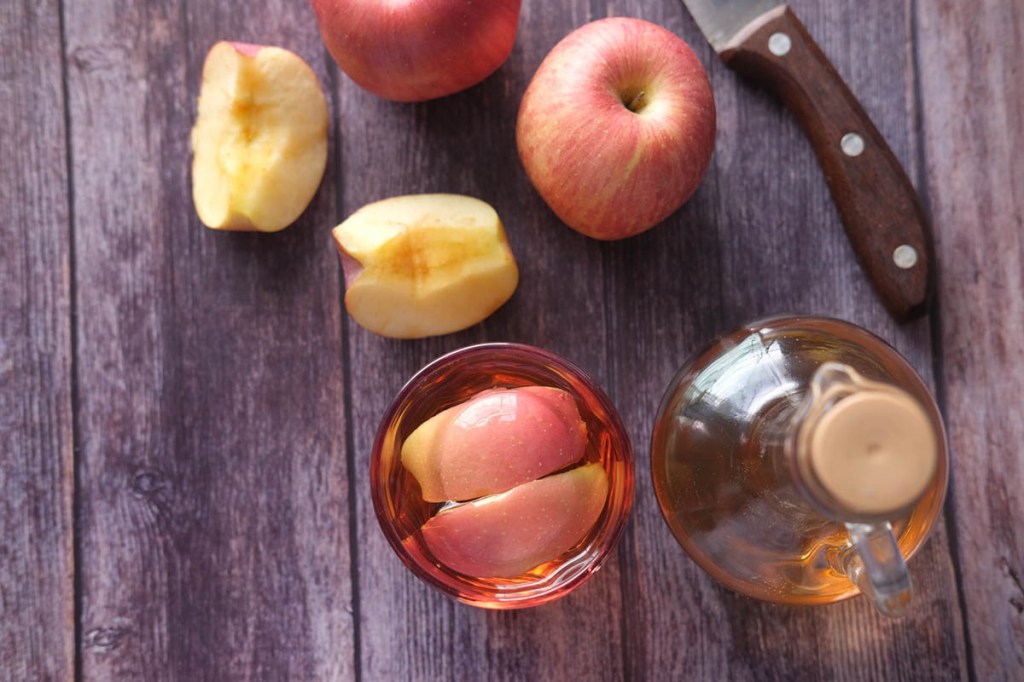Frasco de vidro com vinagre com maçã cortada em mesa de madeira