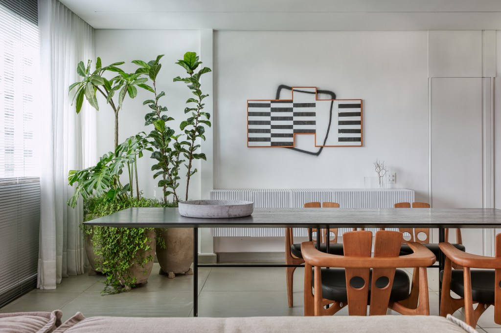 Sala com mesa e cadeiras em madeira; plantas; pintura na parede