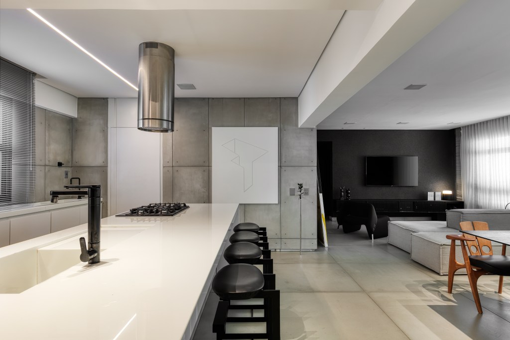 Cozinha minimalista com bancada branca; sala de tv e jantar ao fundo
