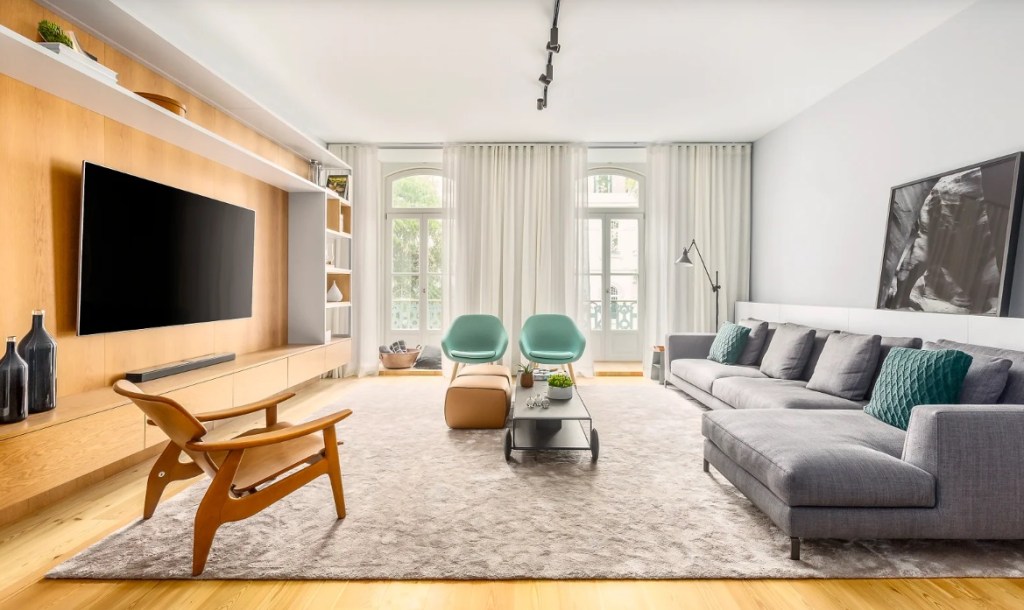 Sala de estar com piso em madeira, sofá cinza e poltrona; Tapete em tom neutro