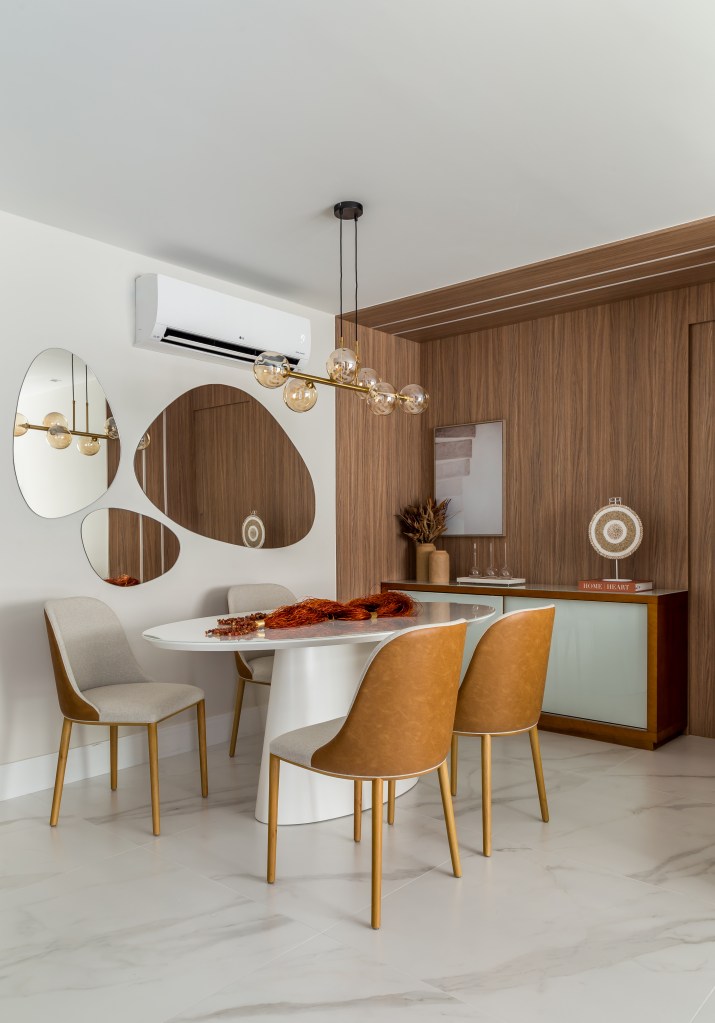 Sala de jantar com mesa oval branca e cadeiras em madeira; espelhos orgânicos na parede